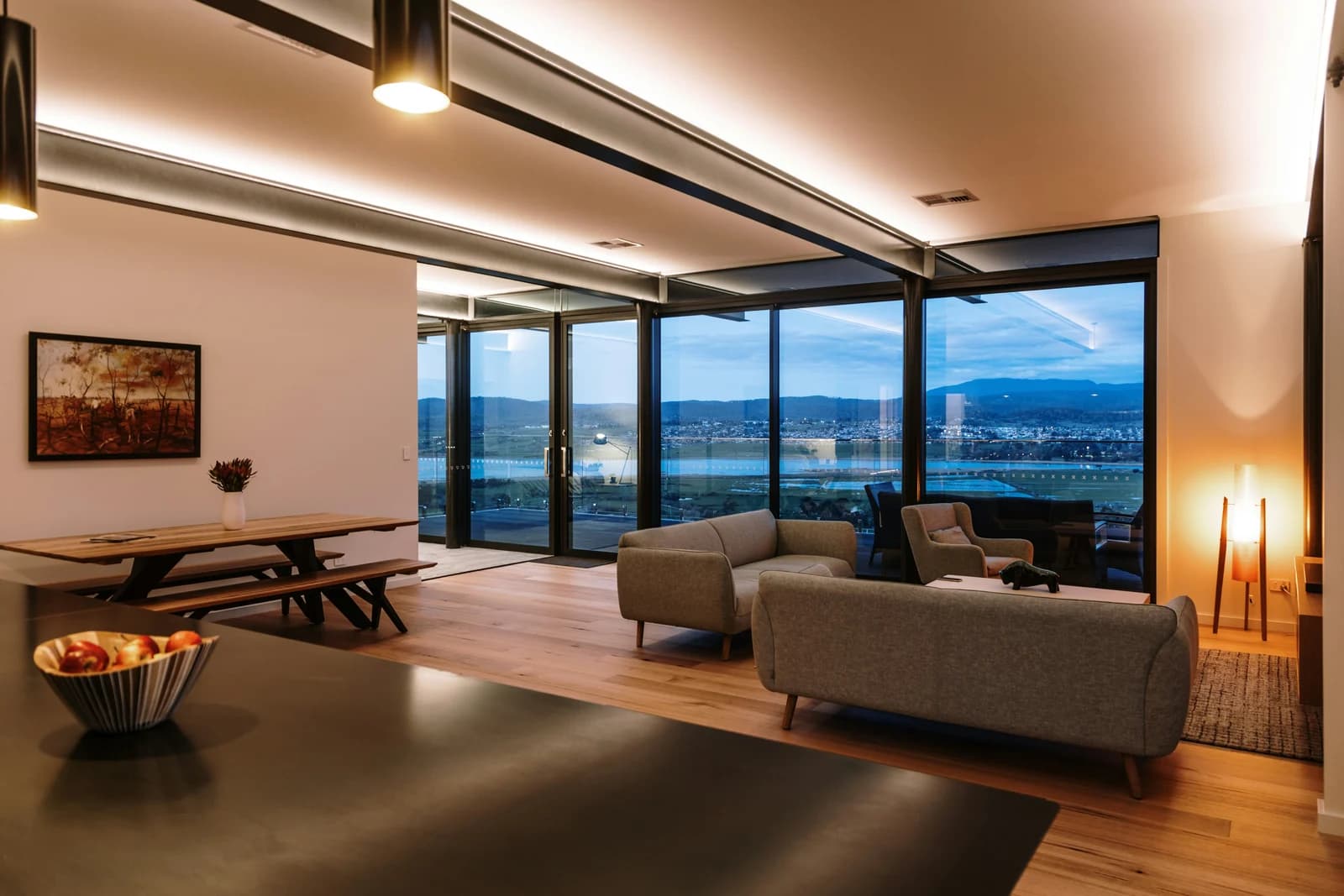 Living room with floor-to-ceiling windows at dusk and a warm floor lamp.