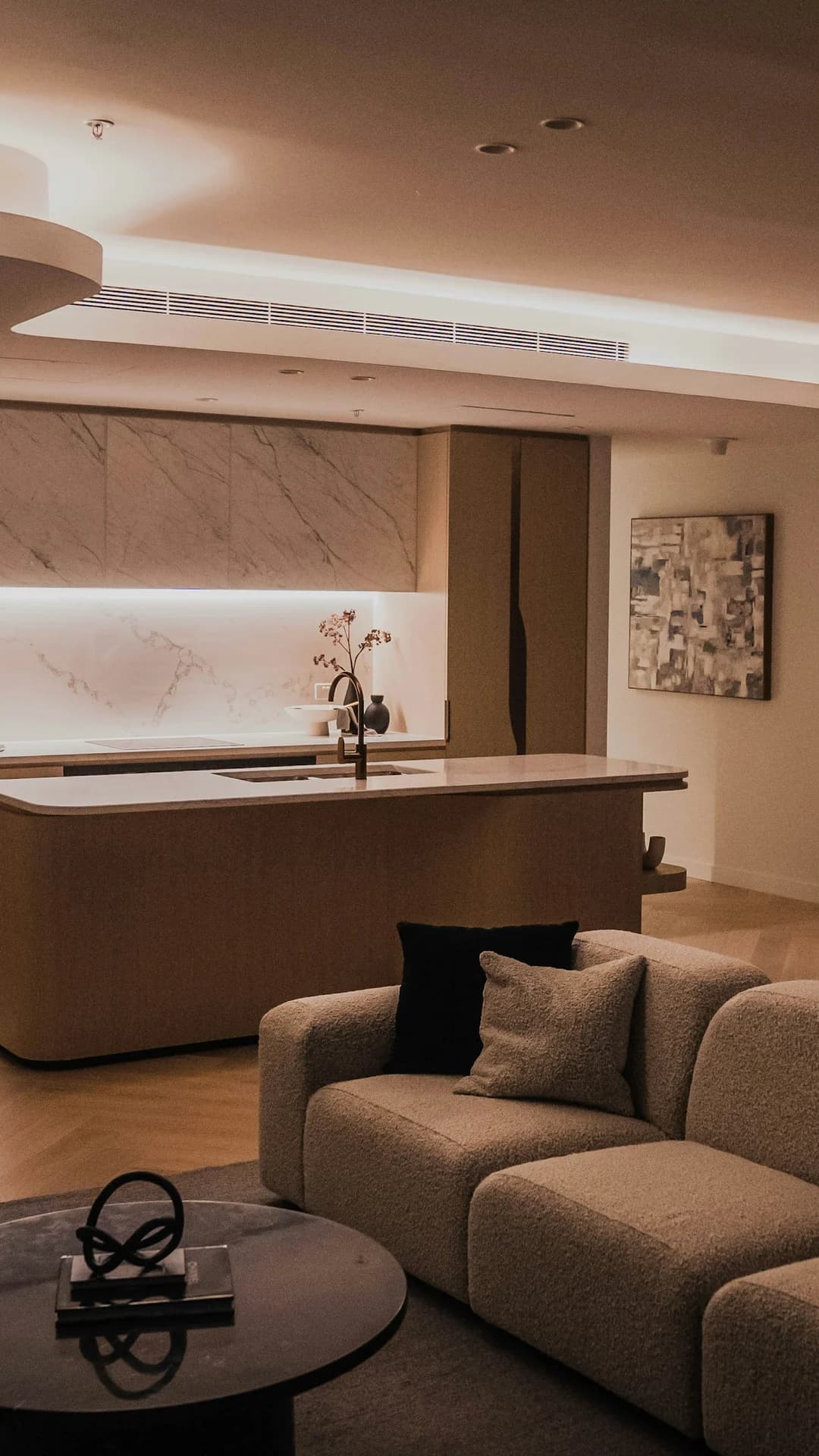 A high-rise living room at night: a soft sofa, round coffee table and city lights through tall glass.