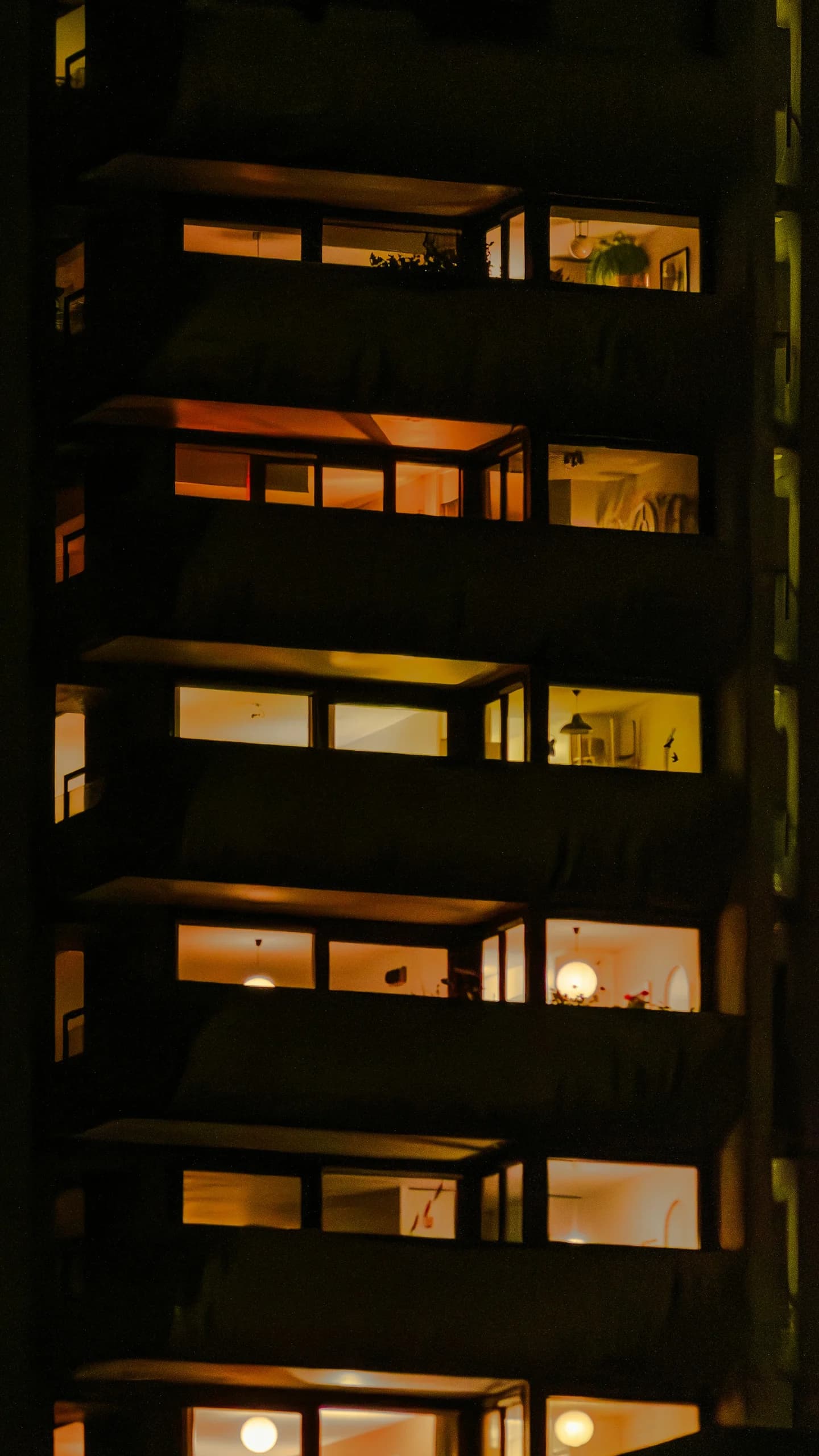 Stacked apartment balconies glowing amber at night; one residence is outlined.